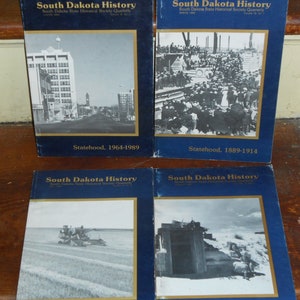 May include: Four copies of "South Dakota History" quarterly journals. The covers are dark blue with black and white images and text. The titles include "Statehood, 1964-1989" and "Statehood, 1889-1914".