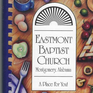 May include: A cookbook with a blue and white cover featuring a church logo and the text "Eastmont Baptist Church, Montgomery, Alabama, A Place For You!" The cover is decorated with a variety of fruits, vegetables, and other food items.