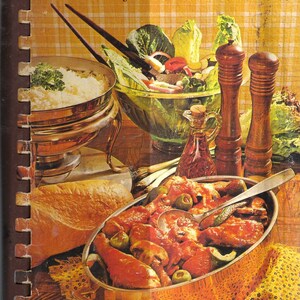 以下が含まれることがあります： 表紙に「Favorite Recipes from our Best Cooks」というタイトルが書かれたビンテージの料理本。表紙には、サラダのボウル、チキンと野菜の盛り合わせ、パン、ご飯のボウル、ペッパーミル2つが置かれたテーブルセッティングの写真が掲載されている。