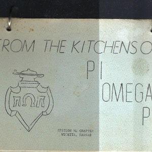 Könnte beinhalten: Ein Vintage-Kochbuchcover mit einer Schwarzweißillustration eines Wappens mit den Buchstaben "ΠΩΠ" darin. Der Text "FROM THE KITCHENS OF PI OMEGA PI EPSILON MU CHAPTER WICHITA, KANSAS" ist auf dem Cover gedruckt.