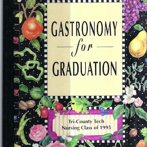 May include: A black and white cookbook with a yellow title card that reads "Gastronomy for Graduation". The title card is surrounded by a black and white checkered border. The cover is decorated with colorful illustrations of fruits, vegetables, and flowers.