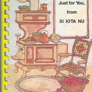 Pode incluir: Ilustração de capa de livro de receitas vintage com uma cena de cozinha com fogão, bule e cadeira de balanço. O texto diz "Just for You, from XI IOTA NU". Uma cesta de maçãs e um tapete completam o design aconchegante.