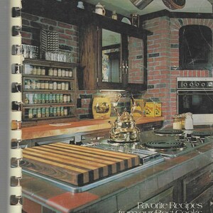 Peut inclure: Couverture d'un livre de cuisine vintage avec une cuisine avec un mur de briques, des armoires en bois et une cuisinière. La couverture indique "Favorite Recipes from our Best Cooks COOK BOOK."