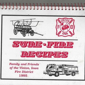 Puede incluir: Un libro de cocina encuadernado en espiral titulado "SURE-FIRE RECIPES" con una portada roja y blanca. La portada presenta ilustraciones de un carro de bomberos antiguo y un camión de bomberos moderno, junto con el logotipo del Departamento de Bomberos de Vinton, Iowa.