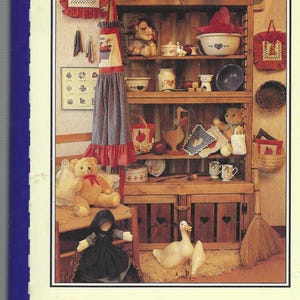 May include: A book titled "Mostly Montgomery: A Collection of Southern Recipes" with a rustic farmhouse-style cover featuring a wooden shelf with various items, including teddy bears, a doll, a broom, and a bowl of fruit.