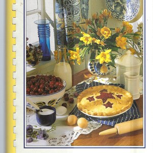 May include: A cookbook titled "Traditions and Treasures: A recipe collection by Providence Baptist Child Development Center" with a photo of a table setting with a cherry pie, a bowl of cherries, a pitcher of milk, a vase of yellow flowers, and a blue and white patterned plate.