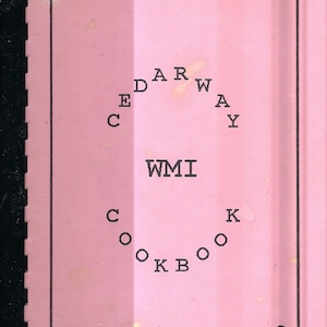 Puede incluir: Portada de libro de cocina rosa con un borde negro y el título "Cedarway WMI Cookbook" en un diseño circular.