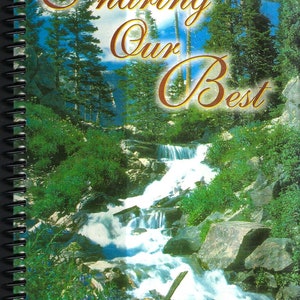 May include: A spiral bound cookbook with a blue sky and waterfall background. The title is "Sharing Our Best" in gold script. The subtitle is "Favorite Recipes and Sayings of Inspiration".