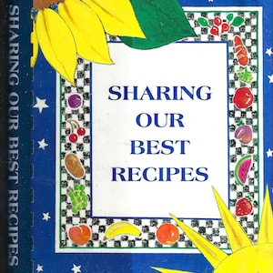 Op de afbeelding: Een blauwe en witte kookboekomslag met een zonnebloem, een zon en sterren. De titel van het boek is "Sharing Our Best Recipes".