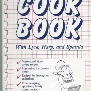 Puede incluir: Portada de libro de cocina con el título "COOK BOOK" en letras azules grandes con contorno blanco. La portada presenta un oso cocinero de dibujos animados y el texto "With Lyre, Harp, and Spatula" y "Richard Gibala". El fondo es una cuadrícula roja.