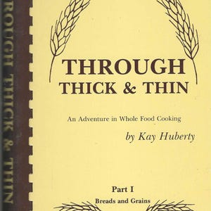 Puede incluir: Un libro de cocina vintage titulado "Through Thick & Thin" con una cubierta de color amarillo claro. El título está en letras grandes de color marrón oscuro, con ilustraciones de trigo. El libro trata sobre la cocina de alimentos integrales.