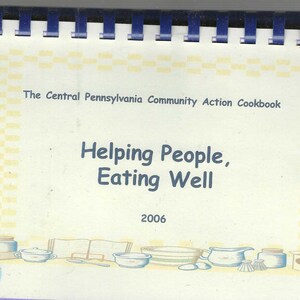 May include: A spiral-bound cookbook titled "The Central Pennsylvania Community Action Cookbook." The cover features the text "Helping People, Eating Well" and the year 2006. Illustrations of kitchenware are at the bottom.