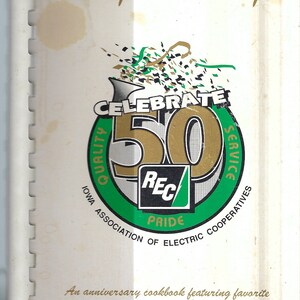 May include: A white cookbook cover with a green and gold logo celebrating 50 years of service. The logo features the text "Celebrate 50" with the words "Quality" and "Service" wrapping around the number 50. The logo also includes the text "REC Pride" and "Iowa Association of Electric Cooperatives". The text "Recipe Roundup" is at the top of the cover. The text "An anniversary cookbook featuring favorite recipes from rural electric cooperative members" is at the bottom of the cover.