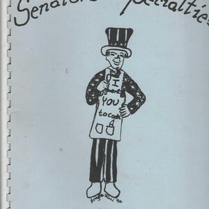 May include: A blue cover with the title "Senators' Specialties" in black cursive writing. A cartoon illustration of a person wearing a hat with stars and stripes, holding a sign that says "I ♥ YOU to cook". The text "A Collection of U.S.A. Senators' Recipes" is at the bottom of the page.