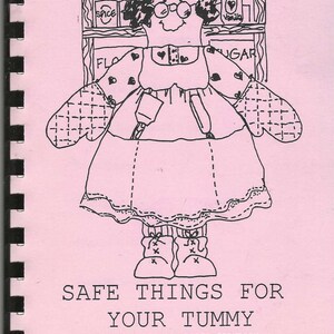May include: A pink cookbook cover with a black and white illustration of a woman wearing an apron and oven mitts. The text "SAFE THINGS FOR YOUR TUMMY" is displayed below the illustration. The cookbook is from the D.C. #99 Safety Committee, 1994.