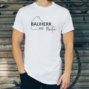 Könnte beinhalten: Weißes T-Shirt mit einer schwarzen Grafik eines Hauses mit dem Text "Bauherr 2024 Martin" darauf.