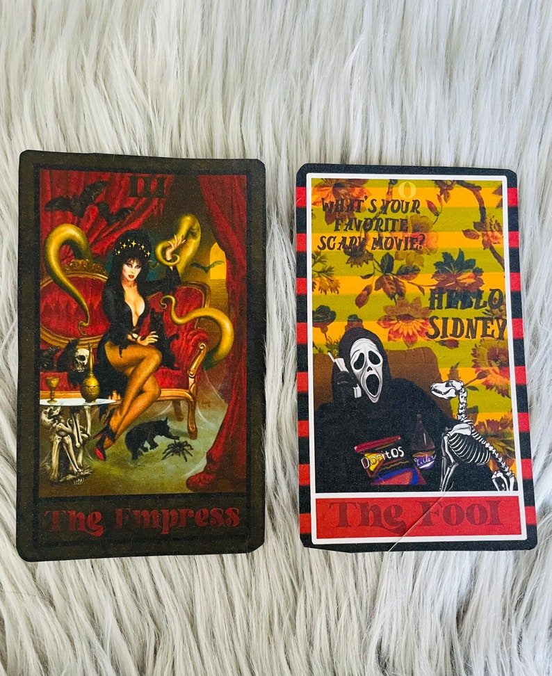 May include: Two tarot cards featuring gothic illustrations. One card depicts a woman in a black dress on a red chair, labeled "The Empress." The other card shows a figure in a Scream mask with the text "What's your favorite scary movie?" and "Hello Sidney," labeled "The Fool."