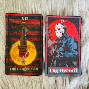 May include: Two tarot cards featuring horror movie characters. One card shows Freddy Krueger as The Hanged Man, the other shows Jason Voorhees as The Hermit. The cards have a red, black, and green color scheme.