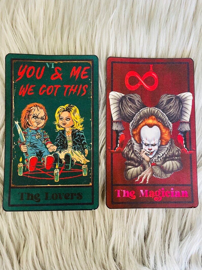 May include: Two tarot cards featuring horror movie characters. One card is green with the text "YOU & ME WE GOT THIS" and images of Chucky and Tiffany. The other card is red with the text "The Magician" and an image of Pennywise.