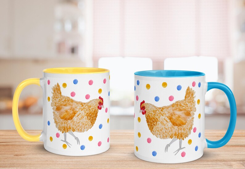 May include: Two ceramic mugs with a white background and colorful polka dots. Each mug features a watercolor illustration of a brown chicken. One mug has a yellow rim and handle, while the other has a blue rim and handle.