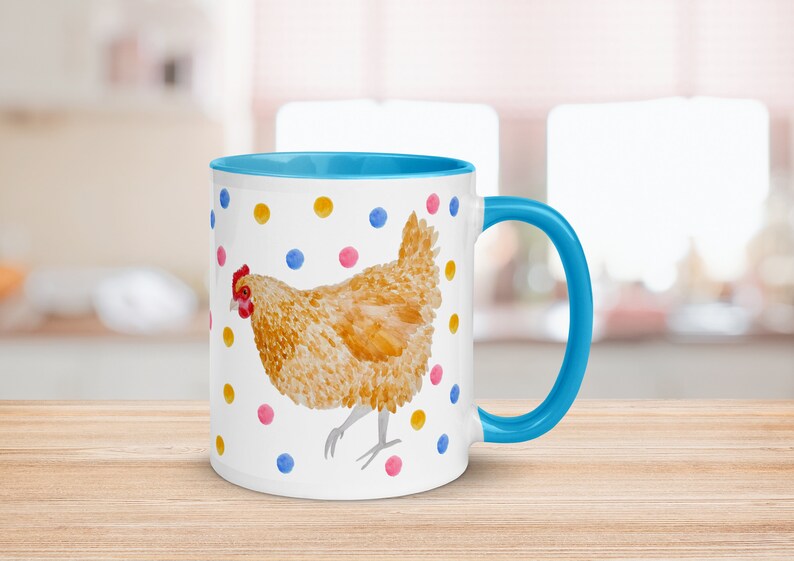 May include: A white ceramic mug with a blue rim and handle. The mug features a watercolor illustration of a brown chicken with a red comb and wattle, surrounded by colorful polka dots.