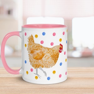May include: A white ceramic mug with a pink rim and handle. The mug features a watercolor illustration of a brown chicken with a red comb walking on a white background with colorful polka dots.