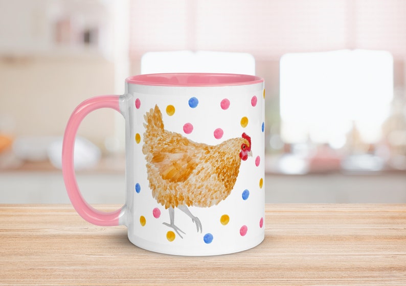 May include: A white ceramic mug with a pink rim and handle. The mug features a watercolor illustration of a brown chicken with a red comb walking on a white background with colorful polka dots.