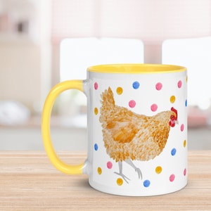 May include: A white ceramic mug with a yellow rim and handle. The mug features a watercolor illustration of a brown chicken with a red comb and wattle, standing on a white background with colorful polka dots.