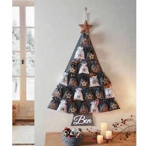 Pode incluir: Um calendário do advento de árvore de Natal de feltro cinza com 24 bolsos numerados. A árvore é decorada com uma estrela dourada e tem o nome "Ben" escrito na parte inferior.