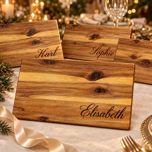 May include: Four rectangular wooden boards with natural grain patterns and dark knots. Each board is engraved with a name in a cursive script: Karl, Sophie, Paul, and Elisabeth. The boards are arranged on a table surface.