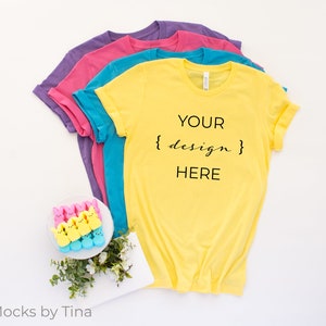 May include: Four blank yellow, turquoise, pink, and purple t-shirts stacked on a white background. The top t-shirt has the text "YOUR {design} HERE" printed on the front.
