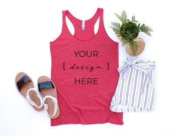 Puede incluir: Camiseta de tirantes roja con el texto "YOUR {design} HERE" sobre un fondo blanco con un par de sandalias, unos pantalones cortos a rayas y una planta en maceta.