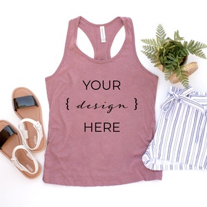 Può includere: Un top a canotta color malva con il testo "YOUR {design} HERE" sul davanti. Il top è appoggiato su una superficie bianca con un paio di sandali bianchi e neri, un paio di pantaloncini a righe bianche e blu e una pianta verde in vaso.