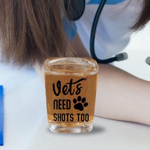 A large 2.2 ounce sized square shot glass that says in a permanent vinyl material, the lettering says, Vets Need Shots Too on the front side of the glass in your choice of colors. The lettering is smooth and will stay on without fading.