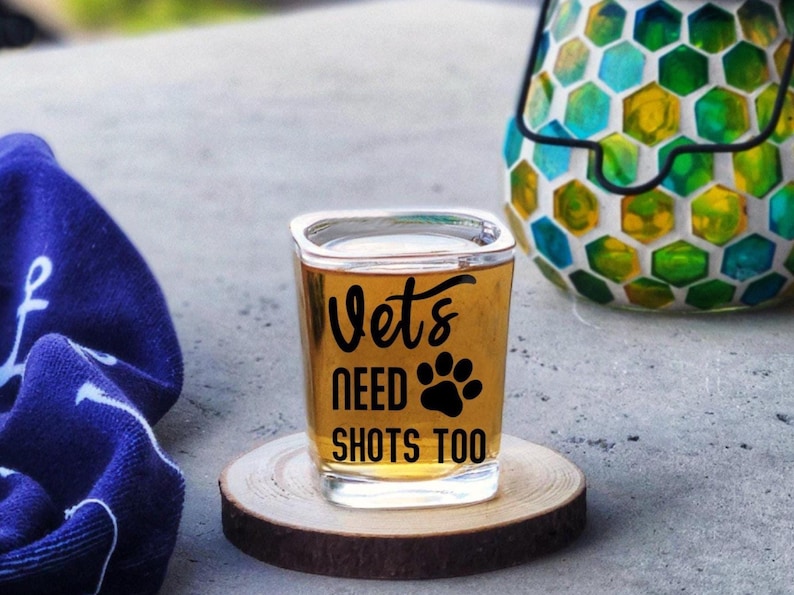 A large 2.2 ounce sized square shot glass that says in a permanent vinyl material, the lettering says, Vets Need Shots Too on the front side of the glass in your choice of colors. The lettering is smooth and will stay on without fading.