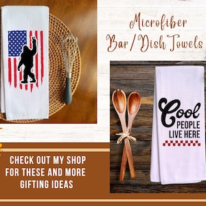 Op de afbeelding: Twee witte microvezel keukendoeken met wafelstructuur. E&eacute;n doek toont een zwart silhouet van een Bigfoot die een vredesteken maakt voor een rood-blauwe Amerikaanse vlag. De andere doek toont de zwarte tekst Cool PEOPLE LIVE HERE boven een rood dambordpatroon.