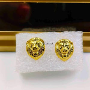 May include: A pair of gold lion head stud earrings. The earrings are small and delicate, and they would make a great gift for a lion lover.