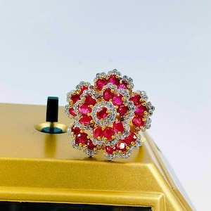 May include: A gold ring featuring a large ruby flower design. The flower is composed of numerous small ruby stones encircled by smaller white diamonds.