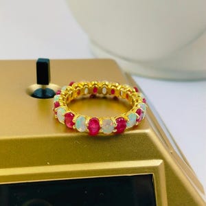 May include: A gold band ring with alternating white opal and red ruby stones.