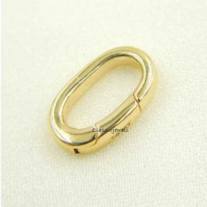 May include: Gold-toned oval-shaped clasp with a spring-loaded closure. The clasp is designed for attaching jewelry or other items.