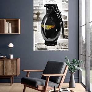 Puede incluir: Una botella negra con forma de granada con un logotipo dorado de Aston Martin sobre un fondo de periódico. El periódico tiene texto que dice "The Aston Martin Challenge for New Owners" y "£475".
