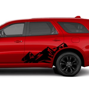 Puede incluir: Un SUV rojo con una calcomanía de cadena montañosa negra en el lateral. La calcomanía es una silueta de montañas con un pico dentado.