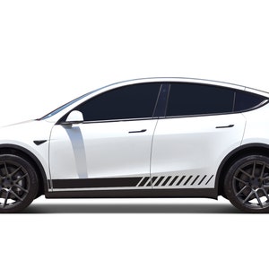 Puede incluir: Vehículo eléctrico blanco con llantas negras y cristales tintados. El coche tiene una franja negra en la parte inferior con un diseño de rayas diagonales. Es un Tesla Model Y.