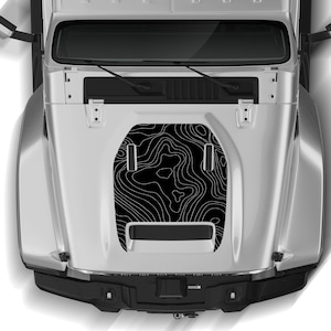 Peut inclure: Un Jeep Wrangler argenté avec un autocollant de capot noir représentant un motif de carte topographique. L'autocollant est composé de lignes blanches sur fond noir.