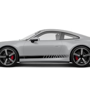 Può includere: Un'auto sportiva argentata con ruote nere e pinze freno rosse. L'auto presenta un design a strisce nere sul lato inferiore. L'auto è su sfondo bianco.