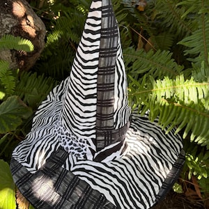 Puede incluir: Un sombrero de bruja caprichoso con un diseño único. El sombrero presenta una combinación de estampados de cebra, cuadros y leopardo en blanco y negro. El ala es ancha y la corona puntiaguda se suma a su estilo distintivo.