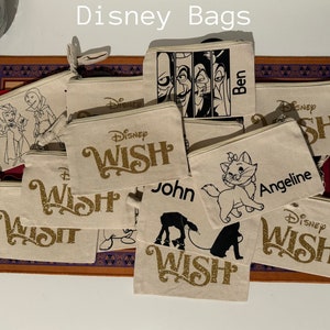 May include: A collection of 12 personalized canvas bags with various Disney characters and names. The bags feature a zipper closure and are decorated with gold glitter lettering. The names on the bags include Ben, Angeline, John, and Wish.