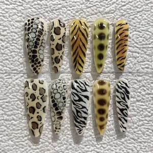 May include: A set of ten long, almond-shaped artificial nails. The nails feature various animal print designs, including leopard spots, tiger stripes, and zebra patterns. The color palette includes shades of brown, black, yellow, and white.