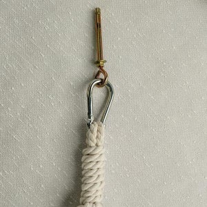 May include: A white cotton rope with a silver carabiner clip attached to a gold metal screw hook.
