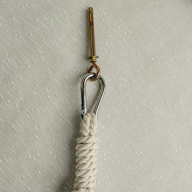 May include: A white cotton rope with a silver carabiner clip attached to a gold metal screw hook.